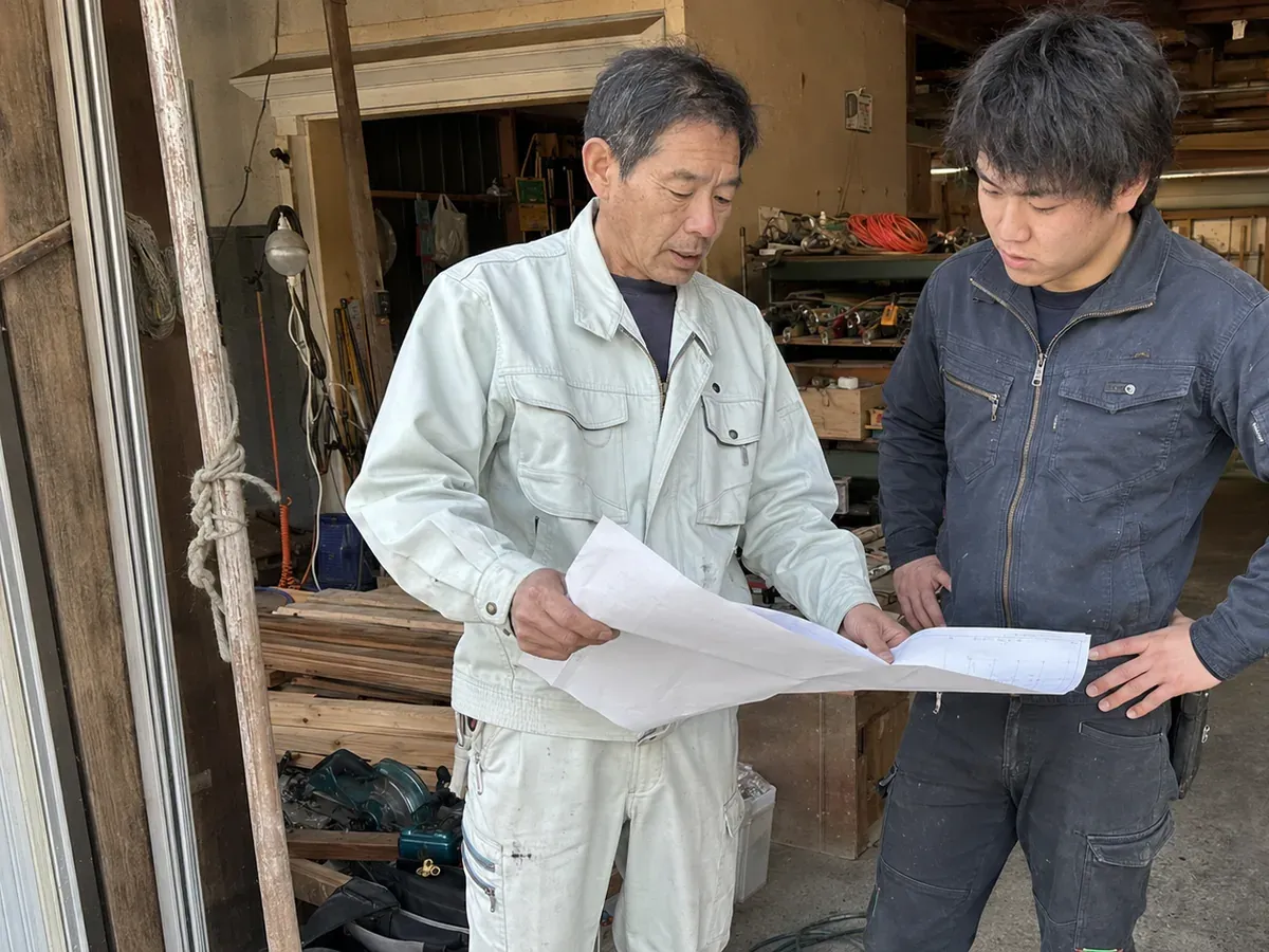 作業場で若手スタッフと図面を確認する田村誠一さん